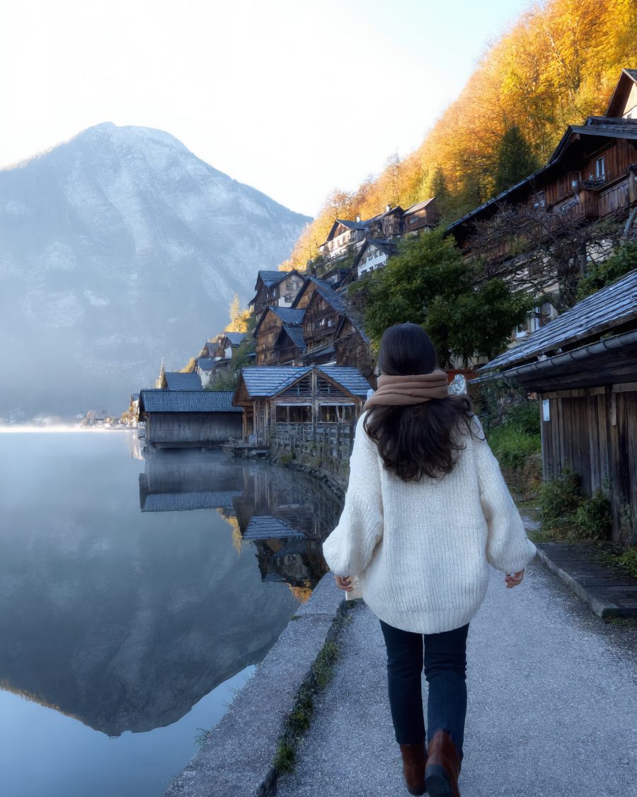 Lia walks the lakeside path in Hallstatt, the mountain reflected in the water.